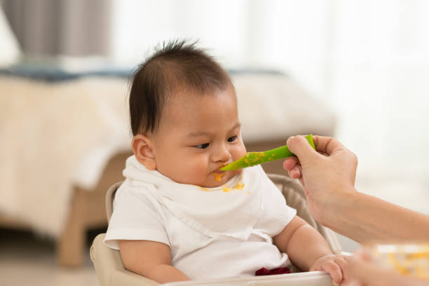 istock Side view mother feeding her asian baby daughter with pumpkin mashed or vegetable mash on rubber spoon.Mom trying to feed little baby boy at home enjoy and spending time together.Baby feeding Concept 1391976745