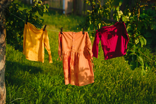 Children's colored clothes dry on clothesline in the garden in nature under rays of the sun after laundering . Protection against fading of colored fabrics. Organic baby washing powders and detergents