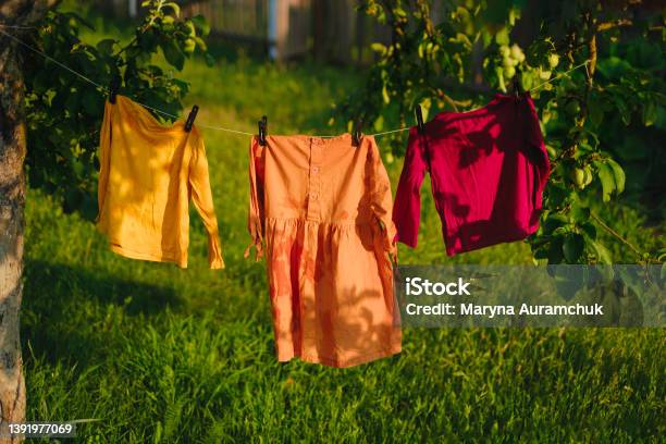 Childrens Colored Clothes Dry On Clothesline In The Garden In Nature Under Rays Of The Sun After Laundering Protection Against Fading Of Colored Fabrics Organic Baby Washing Powders And Detergents Stock Photo - Download Image Now