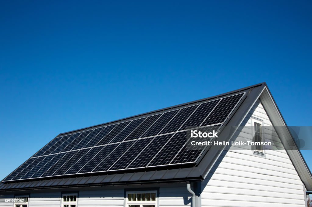 Solar panels on small wood board domestic house roof, sustainable energy concept. Lot of copy space on clear blue sky. Solar Panel Stock Photo