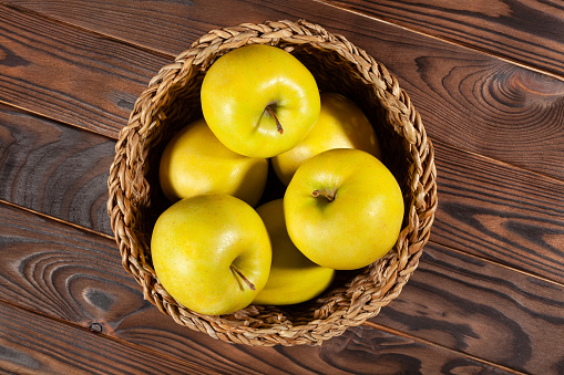 yellow apples in basket on brown wood background top view