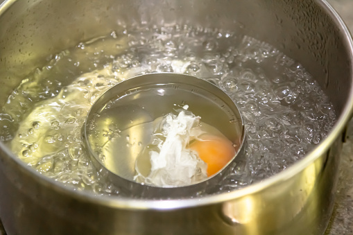 Poaching fresh eggs in a pan of water in an authentic kitchen environment. Four eggs part way through being cooked.