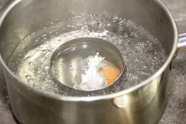 istock Poaching fresh eggs in a pan of water in an authentic kitchen environment. 1391983722