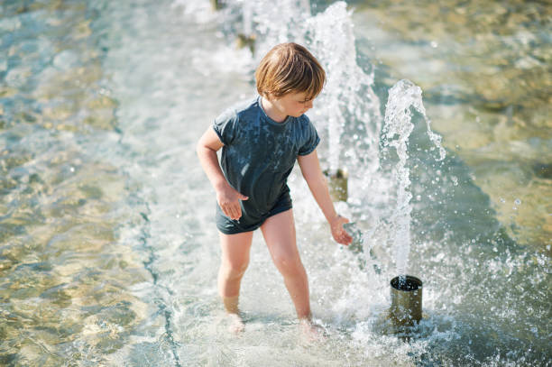 Outdoor portrait of happy little boy playing inside of city fountain on a hot summer day stock photo