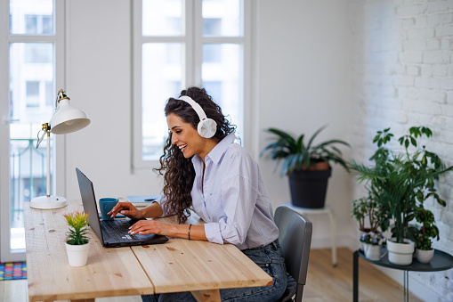 Beautiful young woman in casual clothing using laptop and smiling while working indoors