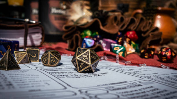 Low angle image of a brass d20 Low angle image of a brass 20-sided die on a character sheet in the sun. In the background are a dice bag and a notebook board game stock pictures, royalty-free photos & images