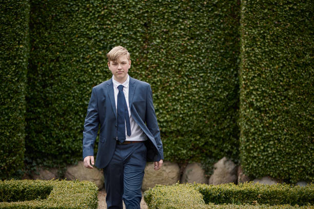 Lutheran Protestant Communion. Portrait of teenager in his confirmation suit. Fourteen year old boy walking towards camera in garden with hedges