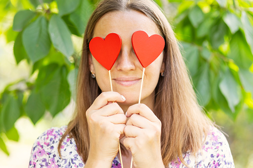 Happy beautiful woman closes her eyes with decorative hearts on the natural backround.