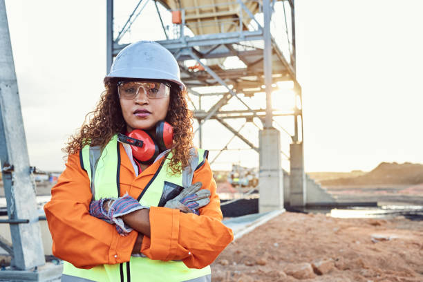 Boss Lady A young African woman mine worker wearing protective wear is looking at the camera with coal mine equipment in the background construction worker stock pictures, royalty-free photos & images