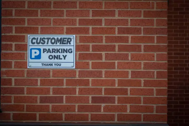 Photo of Customer parking only sign on a red brick wall