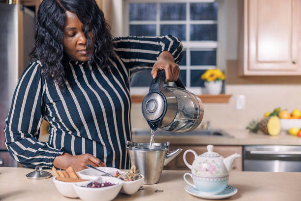 istock A mature attractive Black African-American woman is making herbal tea using a kettle and teapot in her kitchen, pouring the hot water. 1391998029
