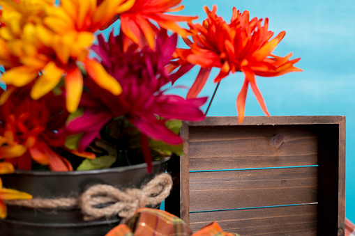 Autumn table decorations.  Bucket of orange flowers,  turquoise background and plaid table runner or cloth.  Empty wooden box for your text.