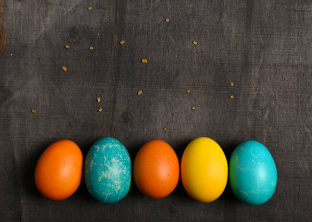 colorful easter eggs arranged in a row on a dark wooden background with blank space for text, easter holiday still life and decoration