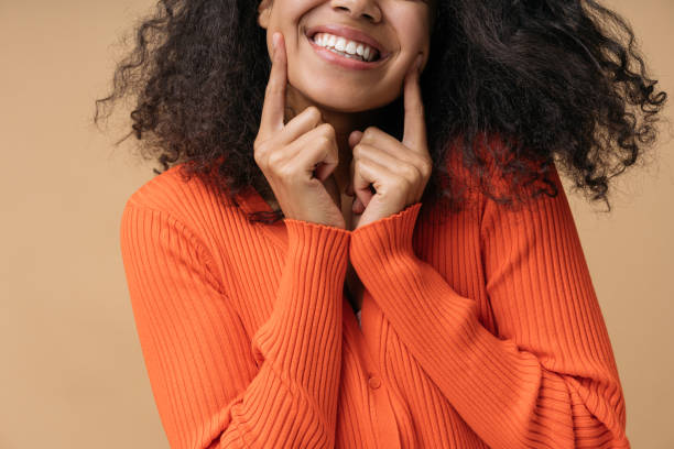 glückliche afroamerikanische frau, die mit dem finger auf weiße zähne zeigt, die auf dem hintergrund isoliert sind. gesundheitswesen, zahnärztliches behandlungskonzept - offenes lächeln stock-fotos und bilder