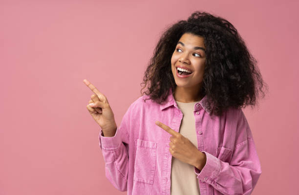 Amazed African American woman wearing pointing finger on copy space isolated on pink background. Shopping, sale, advertisement concept stock photo