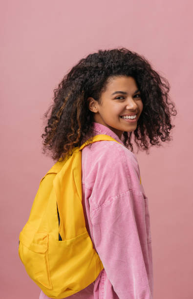 Smiling African American student with backpack looking at camera isolated on pink background. Back to school, education concept stock photo