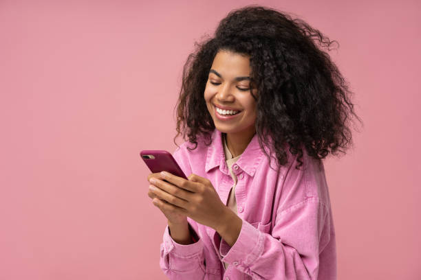 smiling african american woman using smartphone playing mobile game isolated on pink background. happy stylish female holding mobile phone shopping online with sale - färgad bakgrund bildbanksfoton och bilder