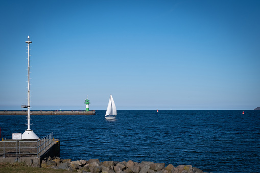 a small white sailboat passes a lighthouse