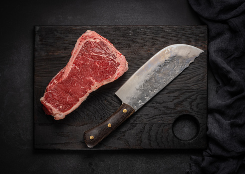 Raw juicy piece of beef meat on the bone lies on a wooden cutting board on a black background. Meat tenderloin New York