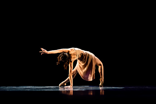 Teenager girl performing contemporary dance on dark stage