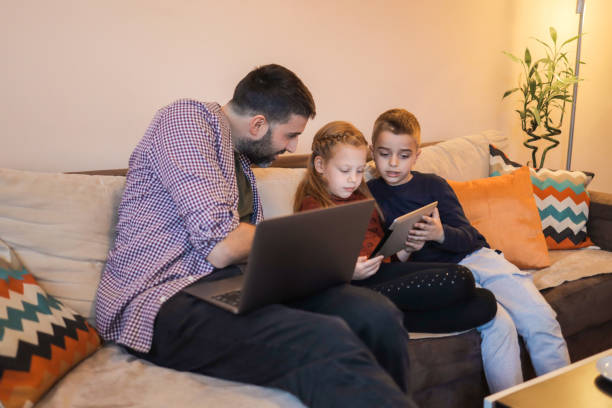istock Father and his two young children using devices at home 1392010020