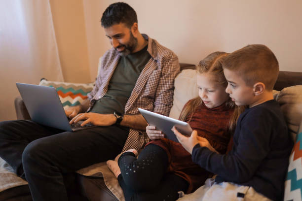 istock Father and his two young children using devices at home 1392010665