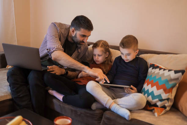 istock Father and his two young children using devices at home 1392010745