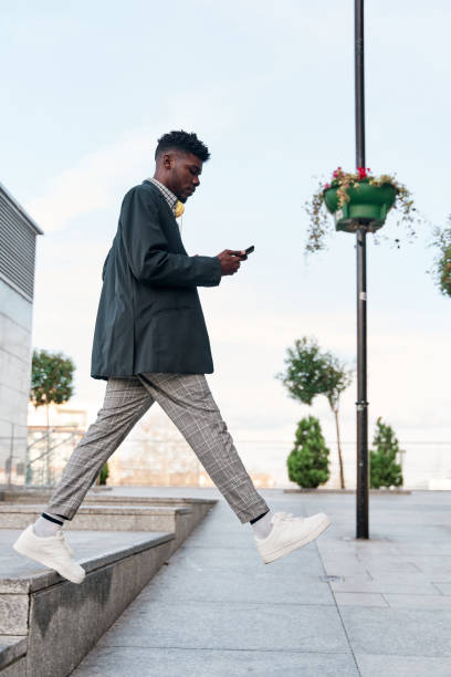 hombre afroamericano con teléfono inteligente caminando sin mirar a dónde va. está a punto de caer. - dropped call fotografías e imágenes de stock