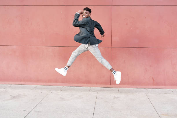 portrait en pied d’un homme afro-américain joyeux sautant isolé sur un fond rouge - hip hop hipster afro men photos et images de collection