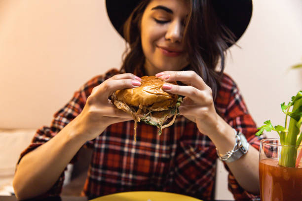 istock Young woman enjoying eating burger and drinking cocktail 1392015424