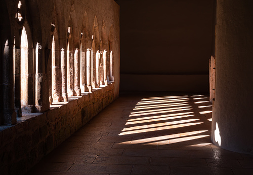 Light shines through openings in the dark convent corridor of Saint Ursanne, Switzerland.