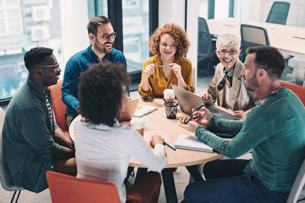 Mixed group of business people sitting around a table and talking Multiracial group of business people having a meeting team stock pictures, royalty-free photos & images