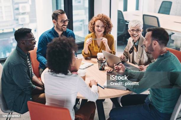Mixed Group Of Business People Sitting Around A Table And Talking Stock Photo - Download Image Now
