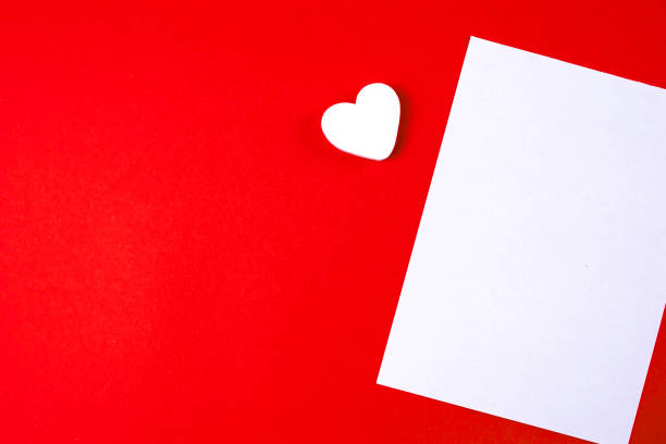 istock Love letter mock up template. Empty blank white paper on red paper background and a white heart with copy space. 1392018224