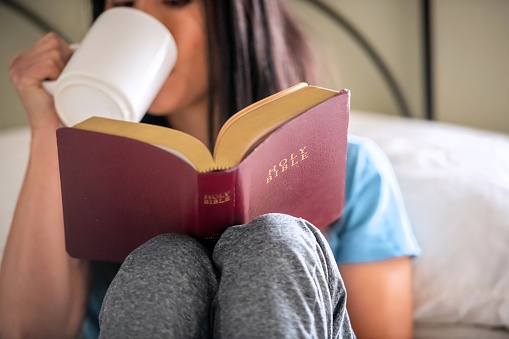 Smiling East Asian woman reading the Bible at home having a cup of coffee