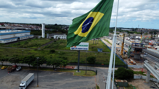 Goiânia, Goias, Brazil – October 18, 2022: Brazil flag fluttering in the wind with Flamboyant flowers on the side and blue sky in the background.