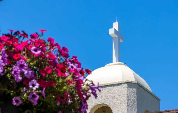 A white Christian cross on the roof of a church with flowers in the foreground.