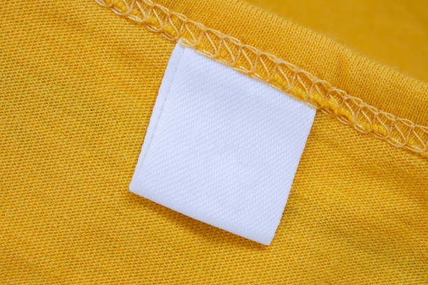 белая пустая этикетка на бирке одежды на фоне ново�й желтой рубашки - label textile shirt stitch стоковые фото и изображения