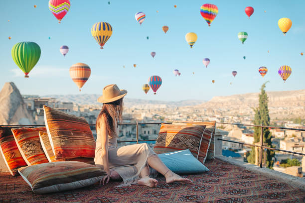 Happy young woman during sunrise watching hot air balloons in Cappadocia, Turkey Young woman in Cappadocia. Woman on a rooftop with air balloons in Goreme in Cappadocia, Turkey hot air balloon stock pictures, royalty-free photos & images