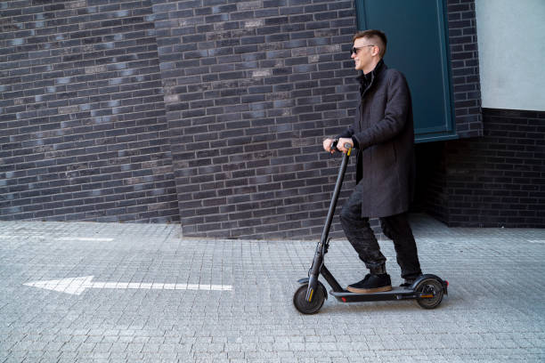 istock Man with e scooter side view, modern building with black bricks in the background 1392043405