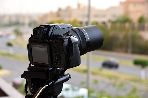 A digital camera fixed on a tripod for time lapse footage and video recording with a blurred top view of a city street and buildings, camera is pointed to the skyline filming the sun, sky and clouds