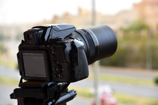 A digital camera fixed on a tripod for time lapse footage and video recording with a blurred top view of a city street and buildings, camera is pointed to the skyline filming the sun, sky and clouds