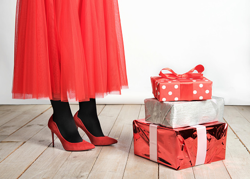 woman wearing red skirt and shoes standing next to stack of red gift boxes. holiday presents. unrecognizable young woman. festive red clothes