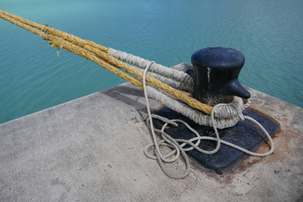 Ship Bollard with attached mooring lines mounted on concrete dock by ocean Ship Bollard with attached mooring lines mounted on concrete dock by ocean mooring line stock pictures, royalty-free photos & images