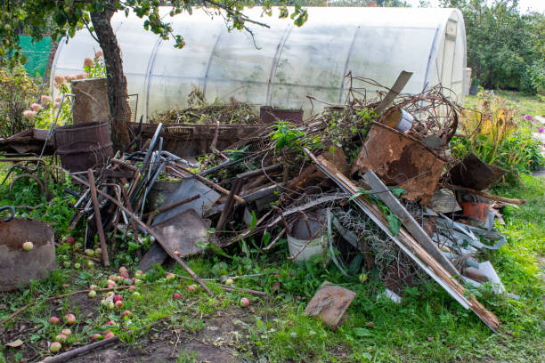 Garbage pile with iron and plastic on the grass. Heap with old rusty iron, tanks, containers, springs. Greenhouse in the country plot.