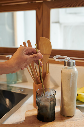 Hand of man putting reusable bamboo straw in glass of protein banana shake