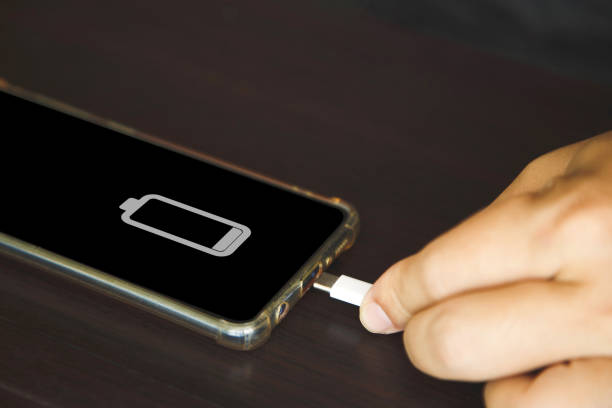 istock Close up a man hands using a USB type C cable to charge mobile phone on wooden table 1392082424