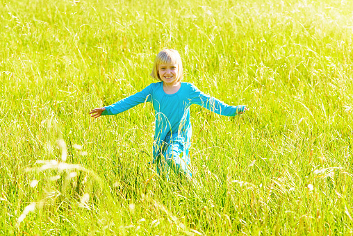 Happy blonde child running and skipping through a beautiful sunlit grass area