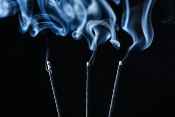 Incense sticks smoldering on black background, closeup