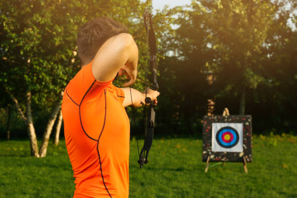 istock Man with bow and arrow aiming at archery target in park, back view 1392090538